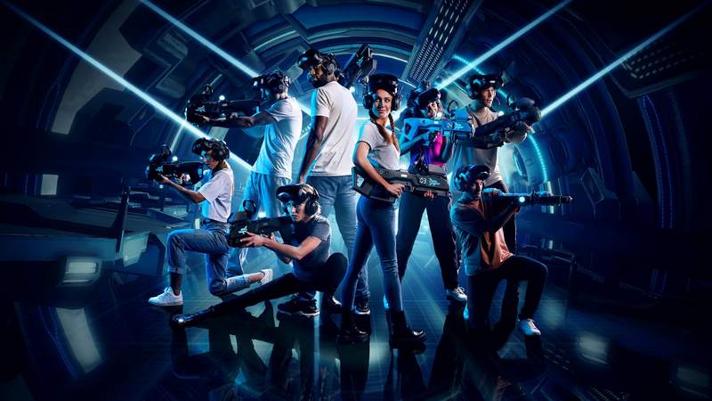 Auf dem Bild ist eine Gruppe von acht Personen mit Virtual-Reality-Brillen und Gewehrcontrollern zu sehen.