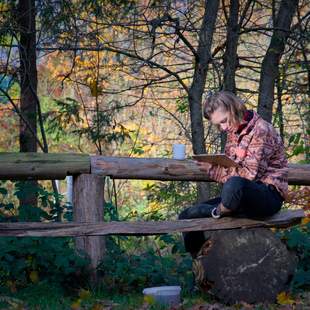 Person sitzt in herbstlicher Natur mit Notizblock und Tasse – Symbol für Reflexion, Ruhe und Selbstführung im Teamkontext.