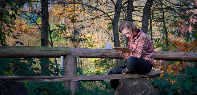 Person sitzt in herbstlicher Natur mit Notizblock und Tasse – Symbol für Reflexion, Ruhe und Selbstführung im Teamkontext.