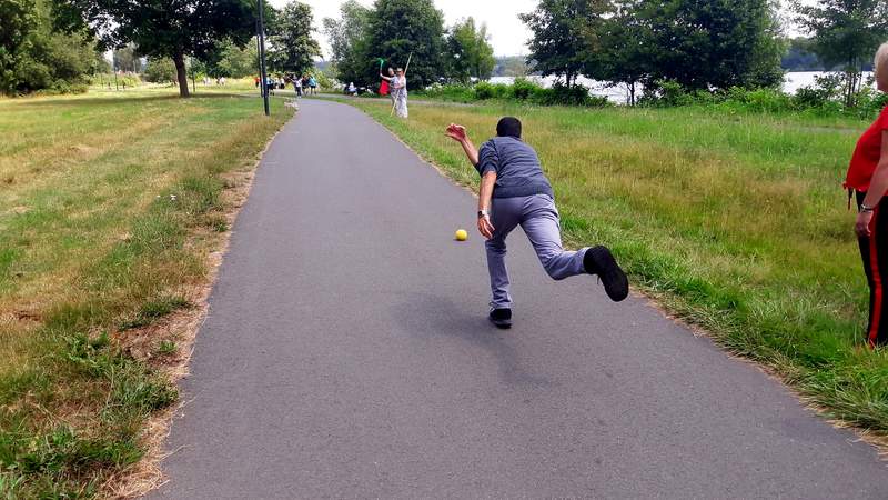 Ein Mensch wirft eine Boßelkugel über den Asphalt