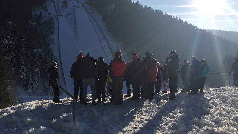 Gäste stehen bei Sonnenschein vor der Skischanze Oberhof.