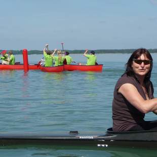 Birgit Fischer sitzt im Kanu auf dem Wasser. Im Hintergrund sieht man mehrere Kanus.