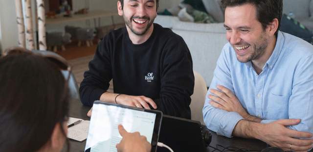 Zwei Männer sitzen an einer KI Station, lachende Gesichter