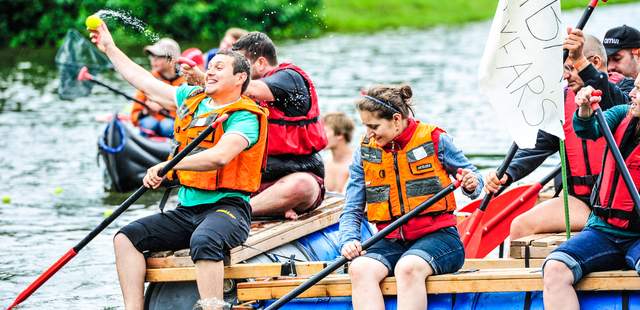 Mitarbeiter paddeln gemeinsam auf einem selbstgebauten Floß beim Firmenevent