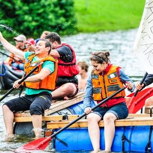 Mitarbeiter paddeln gemeinsam auf einem selbstgebauten Floß beim Firmenevent