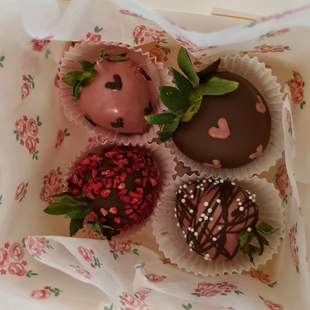 Erdbeeren mit dunkler und rosa Schokolade überzogen, dekoriert mit Herzen und Himbeer-Streudeko.