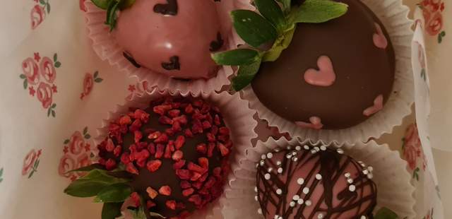 Schokolierte Erdbeeren Erdbeeren mit dunkler und rosa Schokolade überzogen, dekoriert mit Herzen und Himbeer-Streudeko.