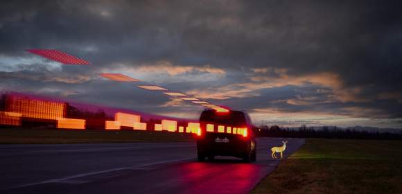 Fahrzeug von hinten auf dunkler Fahrbahn bremst vor Rehatrappe, Bremsllicht als Lichtstrahl.