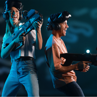 Eine Frau und ein Mann tragen Virtual Reality Brillen und Gewehrcontroller und lachen.