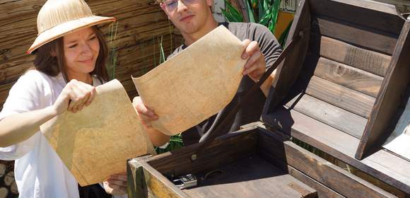 Eine Frau und ein Mann versuchen das Rätsel der Escape Box zu knacken und studieren gerade 2 Pergamente