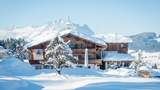 Verschneites Hotel im Bauernhaus Stil in Fieberbrunn mit Bergkulisse im Hinergrund