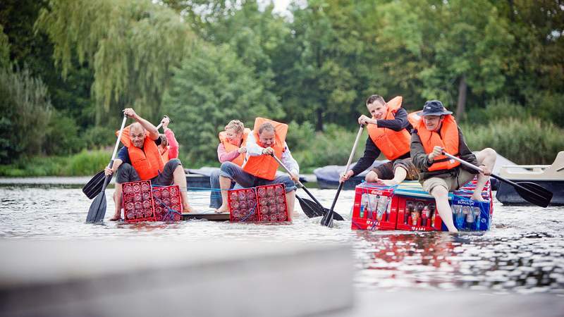 Zwei Flöße aus Colakisten mit Paddlern kommen zum Ufer bei der Firmenfeier mit Floßbauaktion