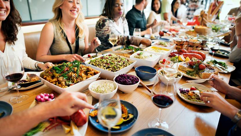 Menschen sitzen am Tisch in fröhlicher Runde und essen gemeinsam.