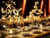 Festlich gedeckte Tafel für eine Weihnachtsfeier mit elegant arrangierten Gläsern und Tellern, umgeben von warmem Kerzenschein und verschwommenen, leuchtenden Weihnachtslichtern im Hintergrund in Form von Sternen und Bäumen.