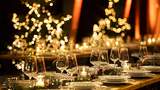 Festlich gedeckte Tafel für eine Weihnachtsfeier mit elegant arrangierten Gläsern und Tellern, umgeben von warmem Kerzenschein und verschwommenen, leuchtenden Weihnachtslichtern im Hintergrund in Form von Sternen und Bäumen.