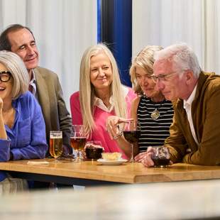 Gruppe von Menschen, die um einen Tisch stehen. Lachend eine Aufgabe lösen
