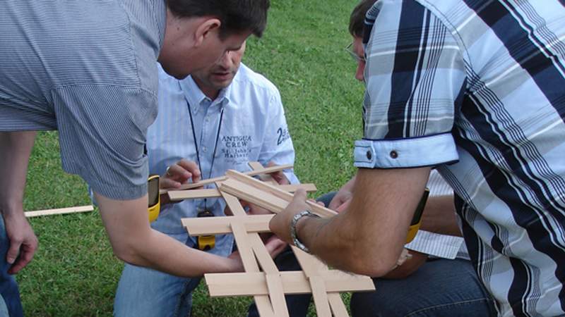 Drei Männer bauen eine Leonardobrücke bei einer Teamentwicklungsmaßnahme