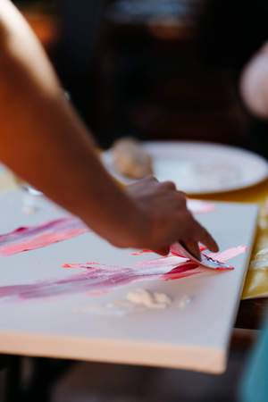 Nahaufnahme einer Hand mit Spachtel beim Malen auf der Leinwand im Workshop