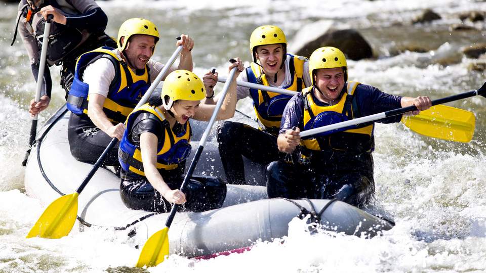 Ein Team sitzt gemeinsam in einem Gummiboot und baddelt einen wilden Fluss entlang