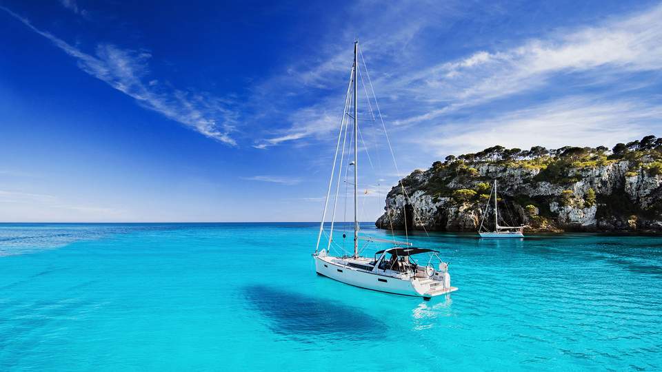 ein Segelboot schwimmt auf hellblauem Wasser vor einer Felsenküsten