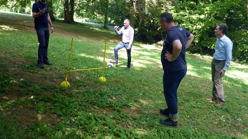 Männer beraten sich beim Fußball-Golf, wie sie den Ball über die Hürde spielen