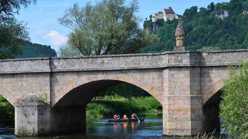 eine familie paddelt unter der nepomukbruecke im hintergrund schloss werenwag