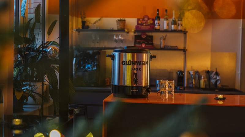 Glühwein-Behälter mit Gläsern daneben auf einer Bar mit gemütlichem Licht im Raum