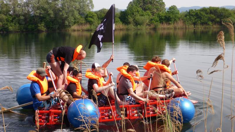 Floß mit Paddlern und Piratenflagge bei Teambuilding Floßbau