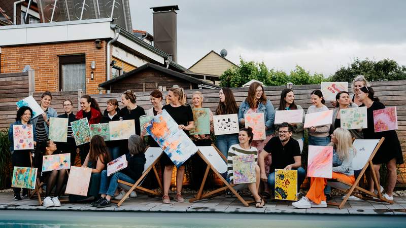 Teamwork trifft Kreativität Gruppe von Teilnehmenden präsentiert stolz ihre abstrakten Kunstwerke nach dem Malworkshop