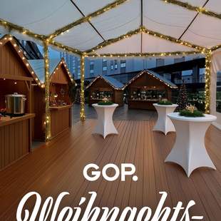 Weihnachtlich geschmücktes Zelt mit Stehtischen und Weihnachtsmarkthütten und dem Schriftzug "GOP Weihnachtsmarkt".