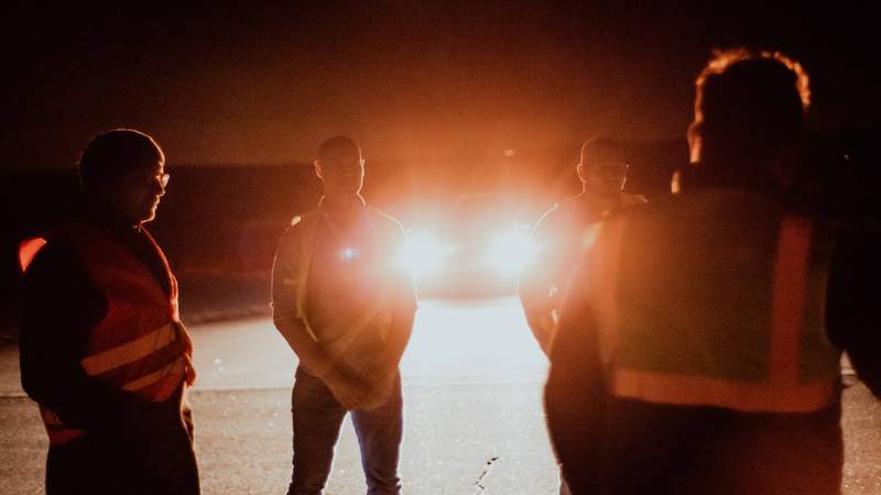 4 Personen stehen Nachts mit Warnweste vor Auto mit Frontscheinwerfer