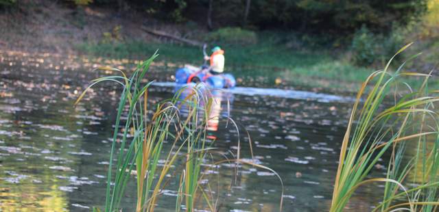 ein Mensch manövriert mit einem Floß aus Fässern über einen Teich