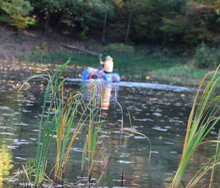 ein Mensch manövriert mit einem Floß aus Fässern über einen Teich