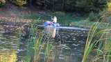 ein Mensch manövriert mit einem Floß aus Fässern über einen Teich
