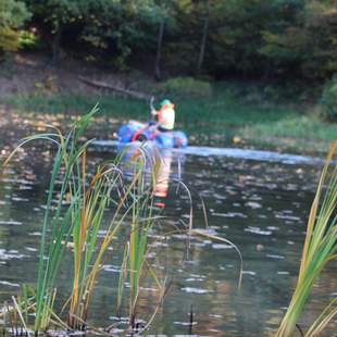 ein Mensch manövriert mit einem Floß aus Fässern über einen Teich