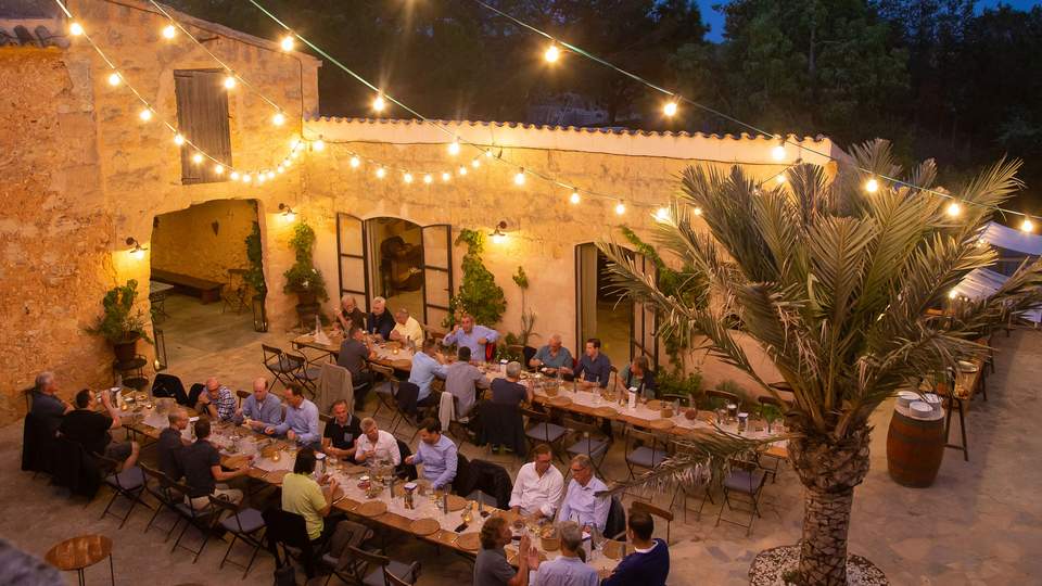 Menschen sitzen an langen Tafeln im Außerbereich einer Location mit Lichterketten-Beleuchtung