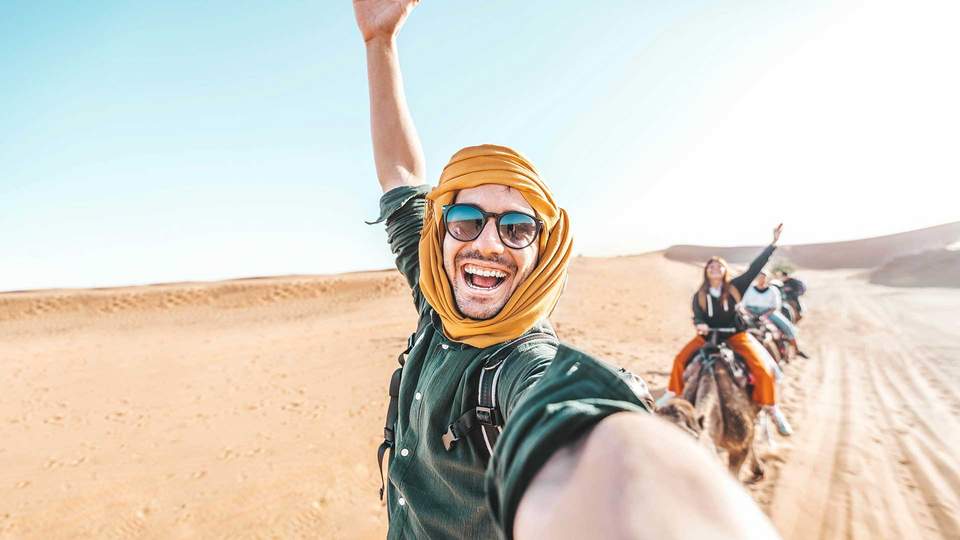 Incentive-Reisen Ausland Mann mit freudigem Gesicht auf einem Kamel in der Wüste reitend.