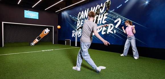 Junge schießt mit orangenen Ball auf den RoboKeeper
