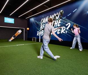 Junge schießt mit orangenen Ball auf den RoboKeeper