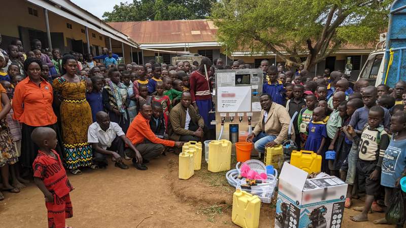 Eine große Gruppe von Kindern und Erwachsenen steht um die Wasserfilteranlage in Uganda