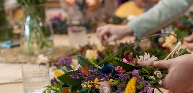 Farbenfroher Blumenkranz Fokus auf die präzise Handarbeit beim Binden eines farbenfrohen Kranzes im StraightCurls Workshop.