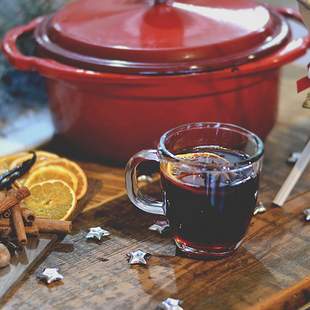 Ein roter Topf mit einem Glas Glühwein und Zimtstangen sowie Orangenscheiben