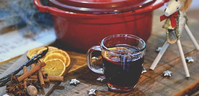 Glühweinkochen als Weihnachtsfeier Ein roter Topf mit einem Glas Glühwein und Zimtstangen sowie Orangenscheiben