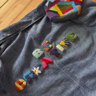 Jeansjacke auf Holzhintergrund mit bunten Punch-Needle-Buchstaben und geometrischen Patches