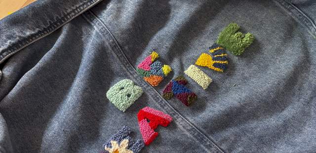 Jeansjacke auf Holzhintergrund mit bunten Punch-Needle-Buchstaben und geometrischen Patches
