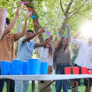 Eine Gruppe von Freunden spielt zusammen Bier-Pong in einer festlichen Gartenlocation
